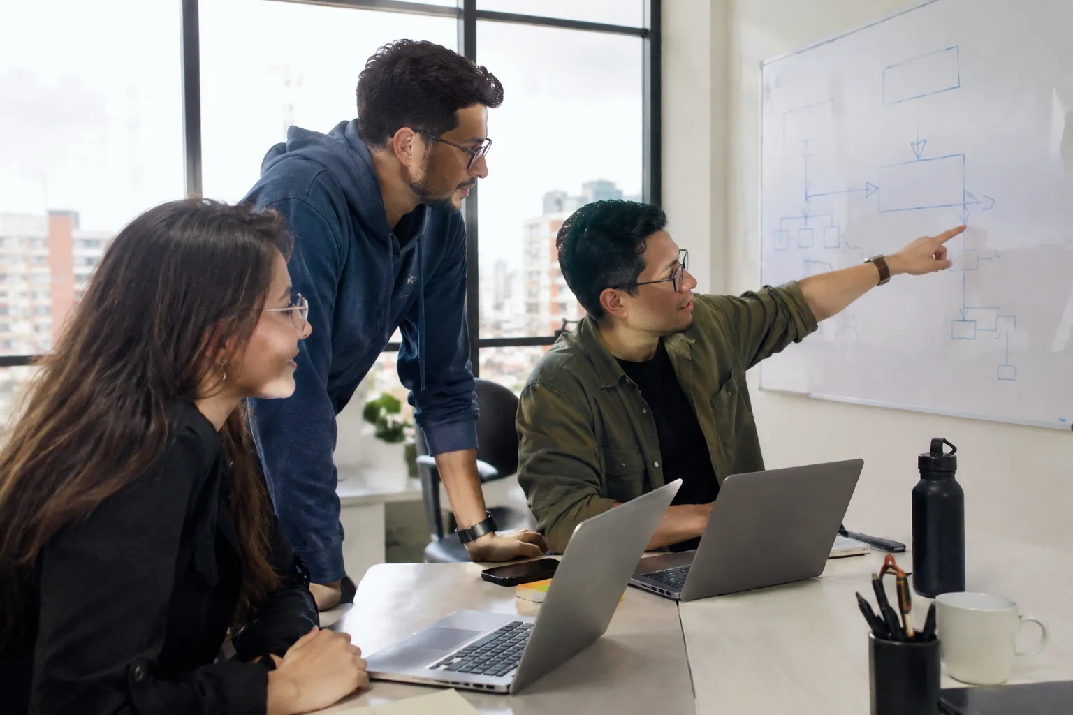 Tres personas del área de tecnología de una empresa frente a un tablero con un diagrama de cajas y flechas